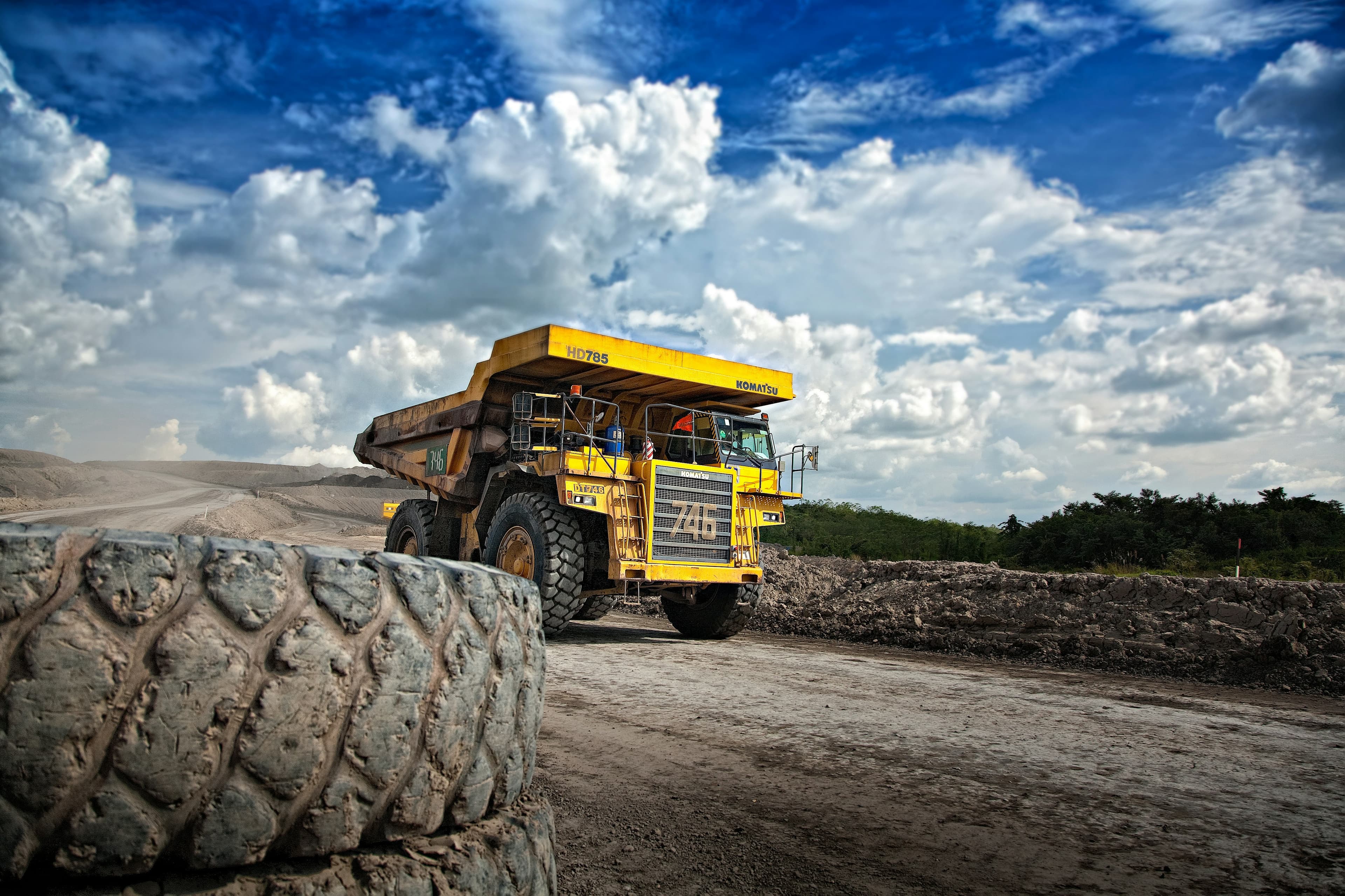 A large yellow mining truck on a dirt road under a blue sky.